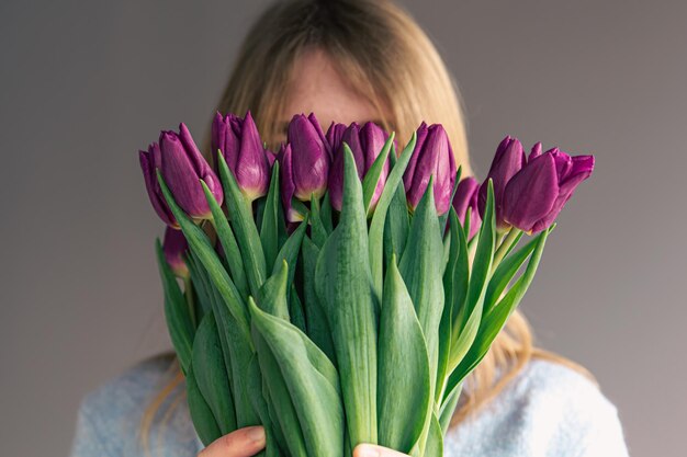 Portrait d'une jeune femme avec un bouquet de tulipes sur fond gris