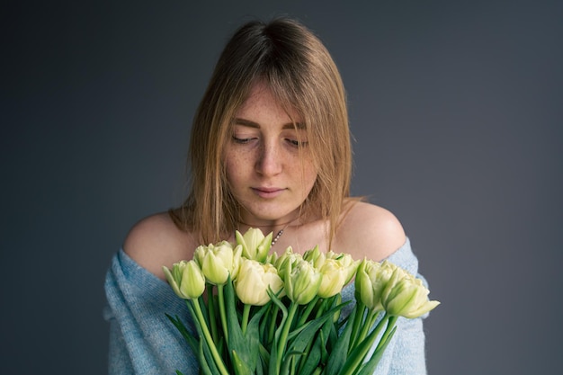 Portrait d'une jeune femme avec un bouquet de tulipes sur fond gris