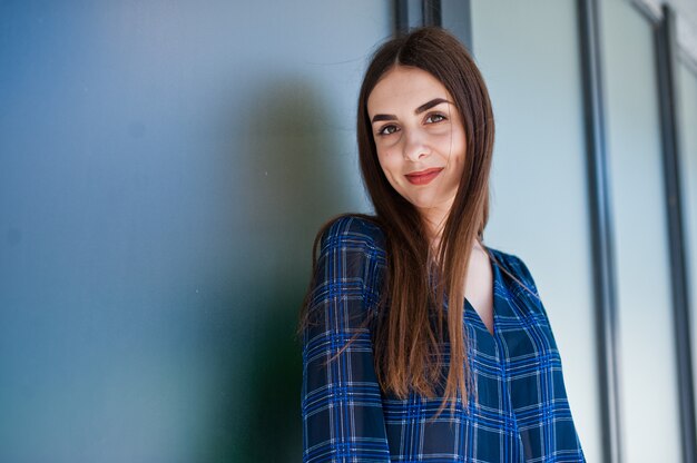 Portrait de jeune femme brune en chemise à carreaux bleu contre les grandes fenêtres.