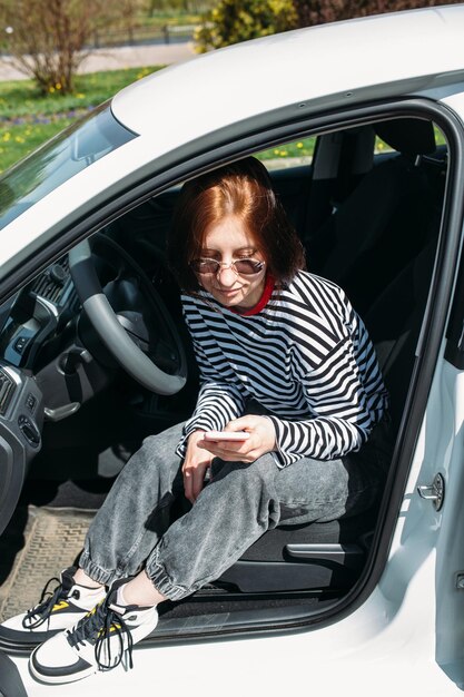 Portrait d'une jeune femme brune conduisant dans une voiture en utilisant un smartphone