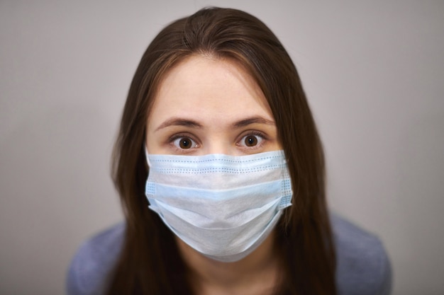 Portrait de jeune femme brune effrayée portant un masque médical de protection, gros plan. Une fille a peur de contracter un coronavirus