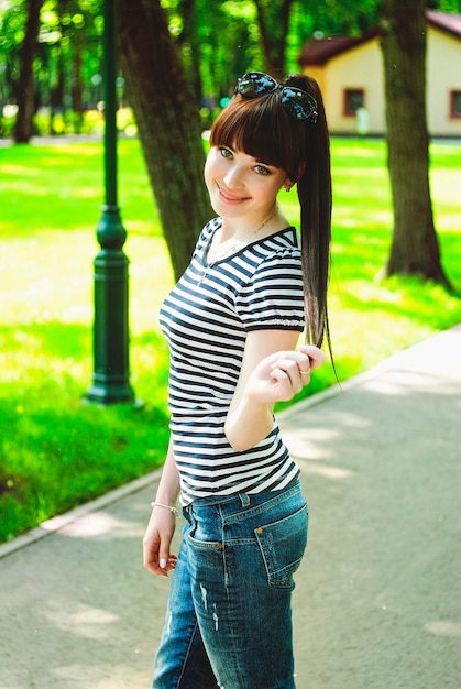 Portrait de jeune femme brune heureuse jeune marchant en jeans dans le parc de la ville. Saison de printemps