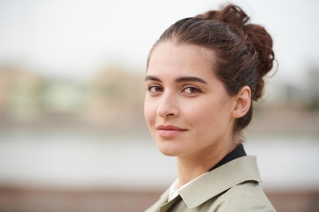 Portrait d'une jeune femme brune en manteau posant sur un fond de ville flou