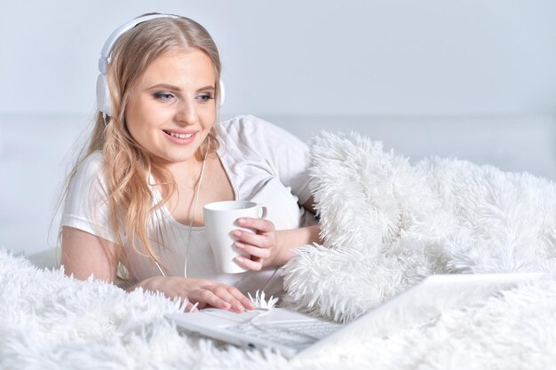 Portrait de jeune femme brune relaxante au lit à l'aide d'un ordinateur portable