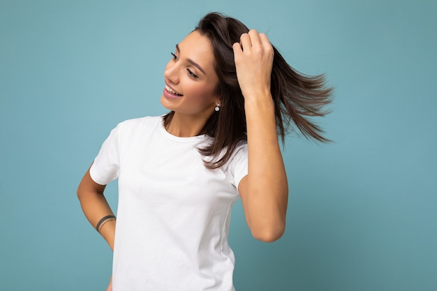 Portrait d'une jeune femme brune souriante à la mode positive et gaie en t-shirt blanc décontracté pour une maquette isolée sur fond bleu avec espace de copie.