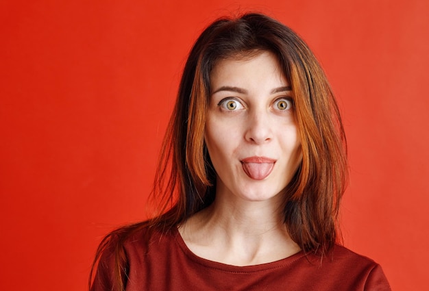 Portrait d'une jeune femme brune vêtue d'un chemisier rouge tirant la langue