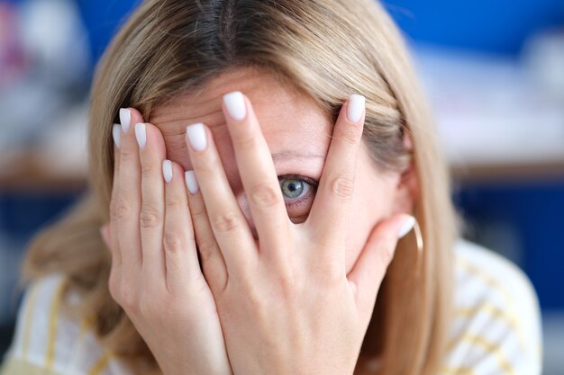 Photo portrait de jeune femme cache le visage et regarde à travers les doigts doute de soi et faible estime de soi