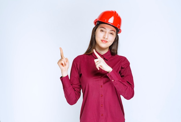 Portrait de jeune femme en casque de protection pointant vers le haut.