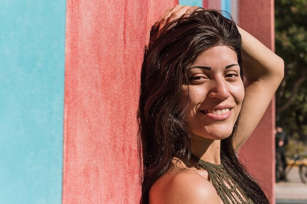 Portrait jeune femme caucasienne appuyée contre un mur en souriant regardant la caméra de la moitié du côté