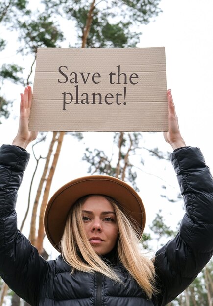 Photo portrait d'une jeune femme caucasienne en chapeau tenant du carton avec du texte à l'extérieur à l'arrière-plan de la nature