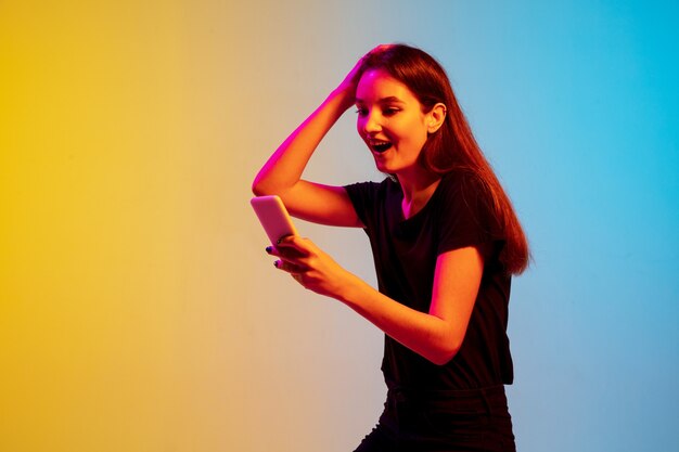 Portrait de jeune femme caucasienne sur fond de studio bleu-jaune dégradé à la lumière du néon