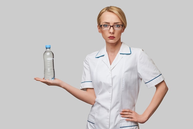 Portrait de jeune femme caucasienne professionnel de la santé tenant une bouteille d'eau debout sur un mur gris clair