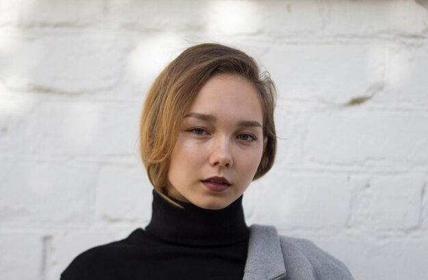 Portrait de jeune femme caucasienne regardant la caméra avec un regard calme sur le fond de briques blanches