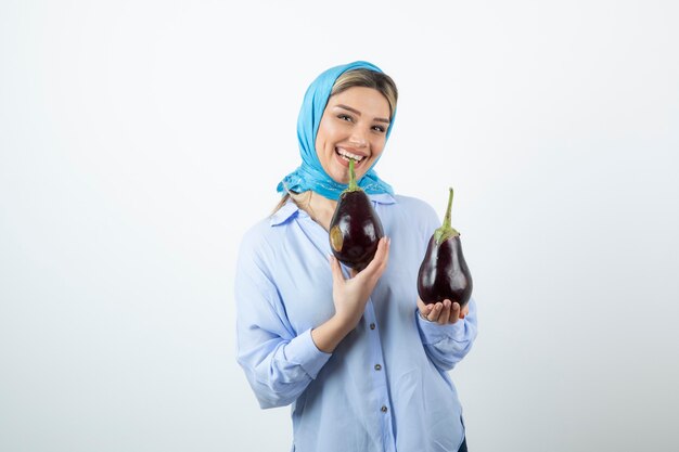 Portrait de jeune femme en châle bleu tenant des aubergines non cuites