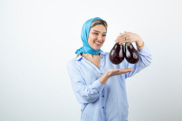 Portrait de jeune femme en châle bleu tenant des aubergines non cuites