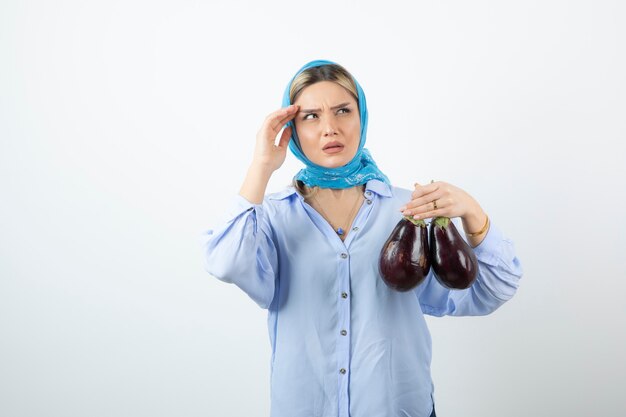 Portrait de jeune femme en châle bleu tenant des aubergines non cuites