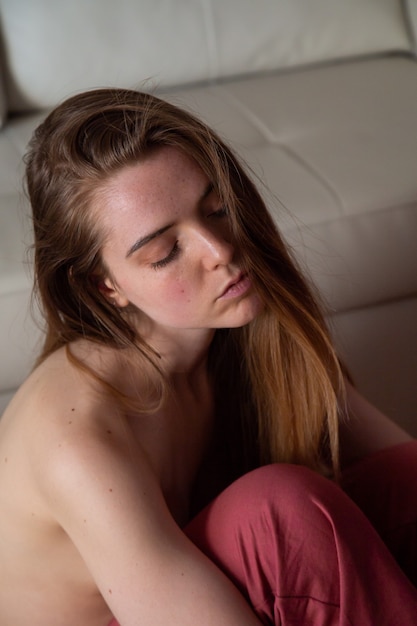 Portrait de jeune femme charmante seins nus aux cheveux bruns, assise sur le sol
