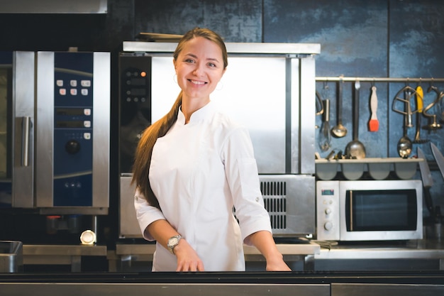 Portrait d'une jeune femme chef confiante et souriante vêtue d'une cuisine professionnelle uniforme blanche sont en arrière-plan