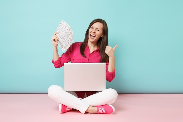 Portrait de jeune femme en chemise rose blouse, pantalon blanc assis sur le sol tenir argent pc