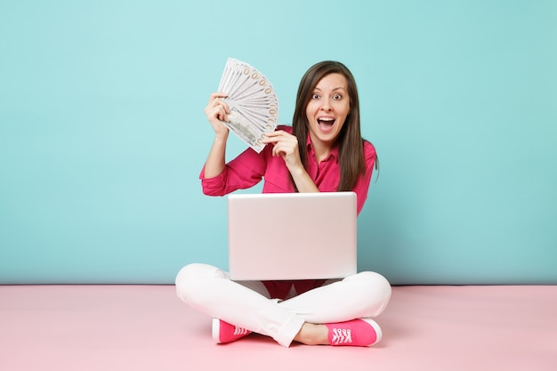 Portrait de jeune femme en chemise rose blouse, pantalon blanc assis sur le sol tenir argent pc