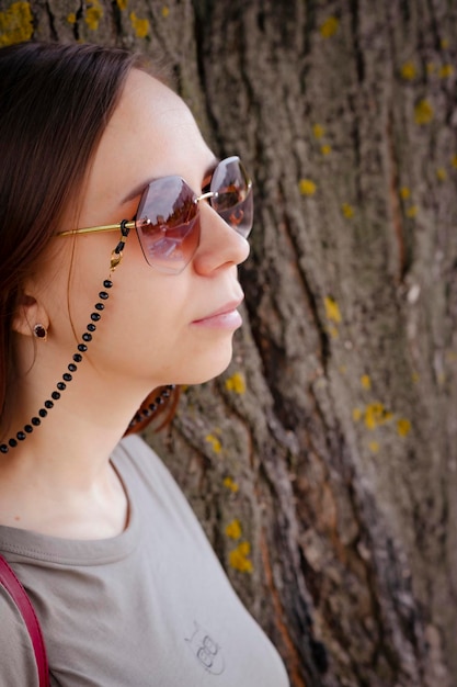 portrait, de, jeune femme, à, cheveux courts, dans, lunettes soleil, regarder loin, debout, s'appuyer, sur, tronc arbre