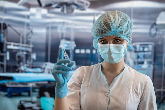 Portrait d'une jeune femme chirurgienne portant un masque chirurgical en tissu de protection dans la salle d'opération