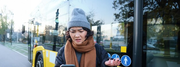 Portrait d'une jeune femme confuse regardant son application pour smartphone avec un visage choqué et déçu