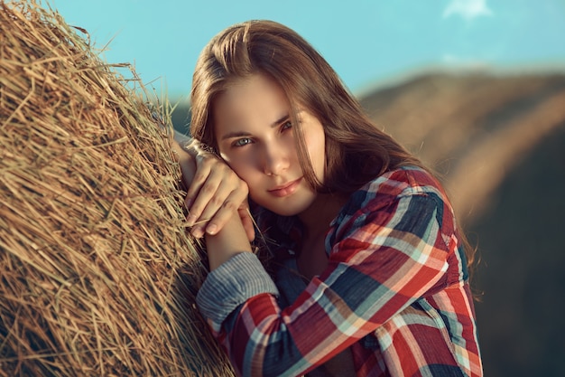 Portrait de jeune femme à côté d'une pile de foin au soleil