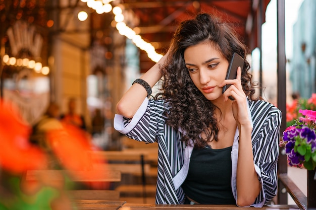 Portrait d'une jeune femme dans un café dans la rue, assis à une table et parlant au téléphone. Concept de mode de vie beauté femme.