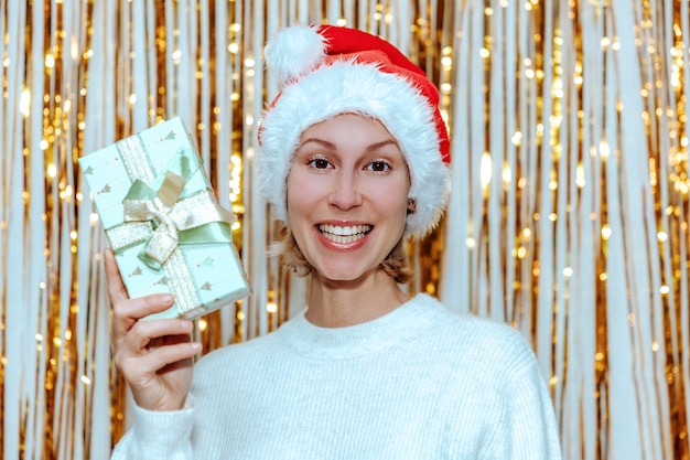 Portrait d'une jeune femme dans un chapeau de père Noël avec un cadeau dans ses mains