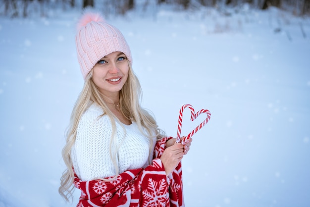 Portrait d'une jeune femme dans un chapeau rose enveloppé dans un plaid rouge à l'extérieur en hiver tenant des sucettes