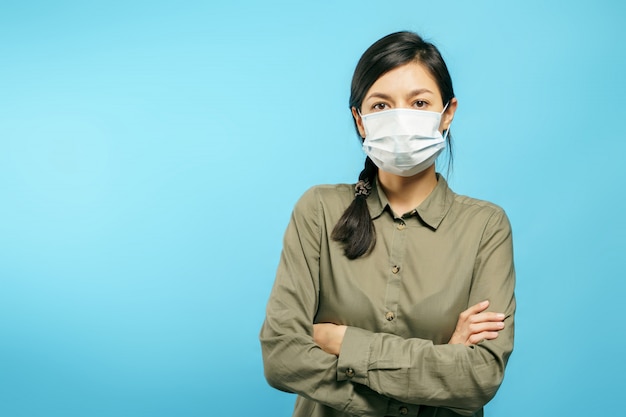 Photo portrait d'une jeune femme dans un masque médical de protection avec les bras croisés sur bleu