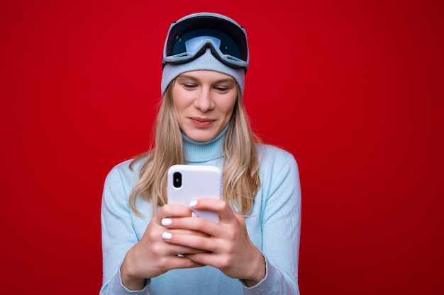 Portrait d'une jeune femme dans un pull et des lunettes de ski avec un téléphone