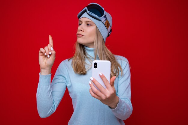 Portrait d'une jeune femme dans un pull et des lunettes de ski avec un téléphone