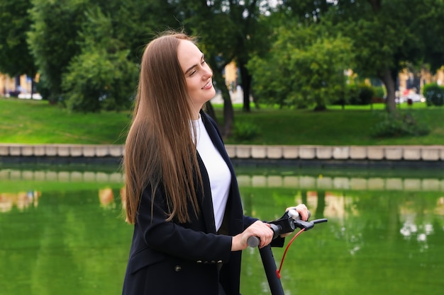 Portrait d'une jeune femme dans des vêtements élégants posant avec un scooter électrique dans la rue