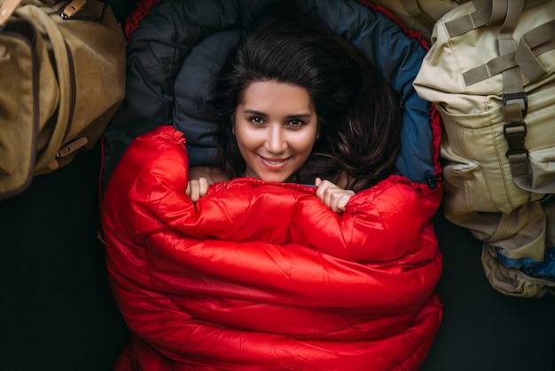 Portrait d'une jeune femme douillette et chaleureuse dans un sac de couchage rouge. Jolie fille touristique avec un sac de couchage rouge dans une tente. Voyage de camping, une femme se reposant dans un sac de couchage. Randonnée, loisirs de plein air