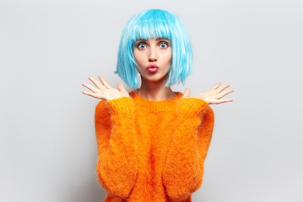 Portrait de jeune femme drôle avec coupe de cheveux bob bleu envoi de baiser soufflant, portant un pull orange.