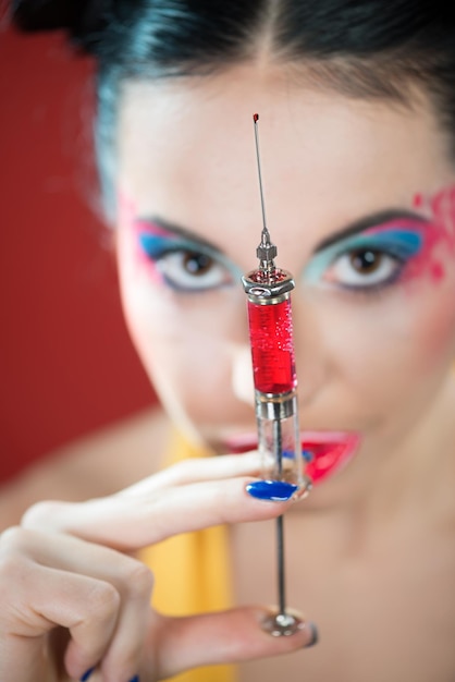 Portrait d'une jeune femme drôle avec un maquillage coloré regardant la seringue dans sa main