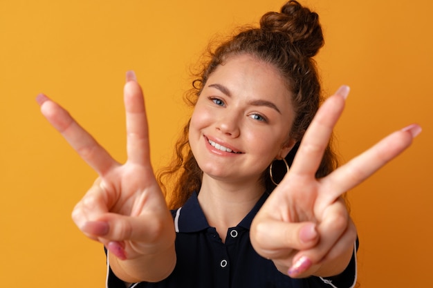 Photo portrait d'une jeune femme drôle montrant un geste de paix sur fond jaune