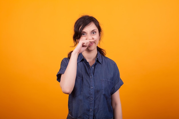 Portrait d'une jeune femme drôle se grattant le nez après avoir utilisé des cosmétiques. Jeune femme faisant un drôle de geste en studio sur fond jaune.