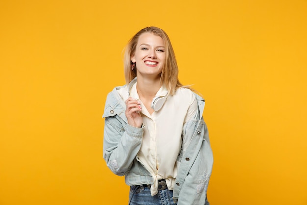 Portrait d'une jeune femme drôle en train de rire dans des vêtements décontractés en denim avec un casque à la recherche d'une caméra isolée sur un fond de mur orange jaune vif en studio. Concept de style de vie des gens. Maquette de l'espace de copie.