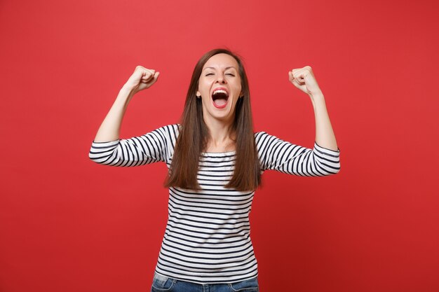 Portrait d'une jeune femme drôle en vêtements rayés écartant les mains, montrant des biceps et criant