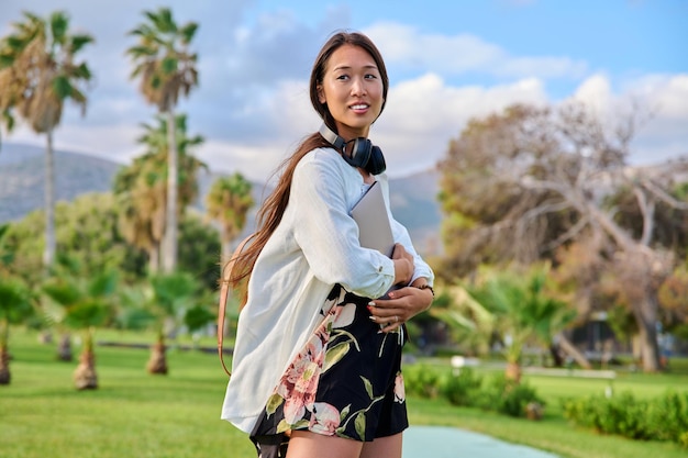 Portrait de jeune femme avec des écouteurs de sac à dos et un ordinateur portable dans ses mains