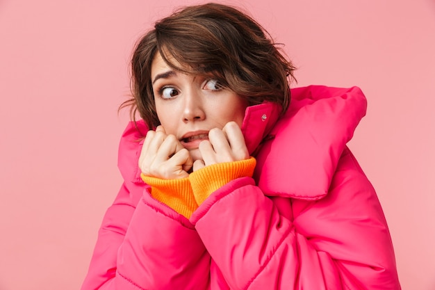 Portrait de jeune femme effrayée en manteau chaud à côté isolé sur rose