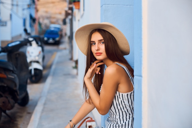 Portrait de jeune femme élégante au chapeau de paille assis dans la rue.