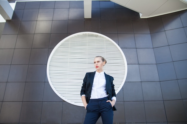 Portrait de jeune femme élégante en costume à l'écart contre la façade de l'immeuble