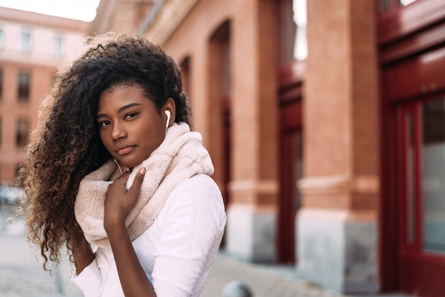 Portrait d&#39;une jeune femme élégante écouter de la musique avec des écouteurs sur la rue de la ville.