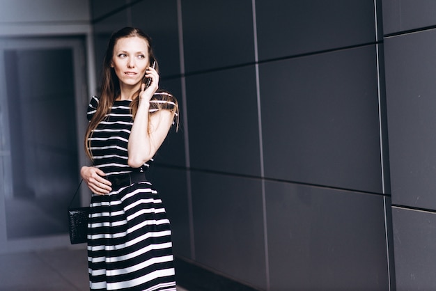 Portrait d&#39;une jeune femme élégante qui marche dans la ville moderne et se présente sur un téléphone mobile