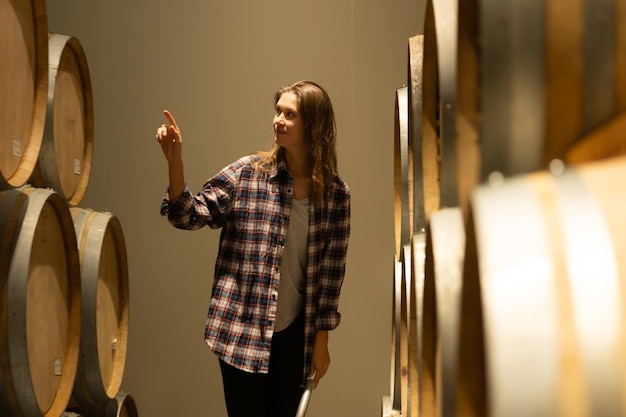 Portrait d'une jeune femme entourée de barils de vin dans sa cave