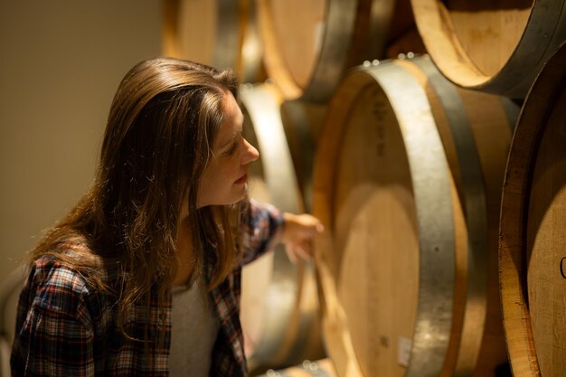 Portrait d'une jeune femme entourée de barils de vin dans sa cave